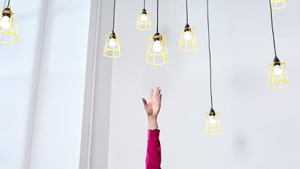 A hand reaching up towards several hanging lightbulbs, trying to grasp one.